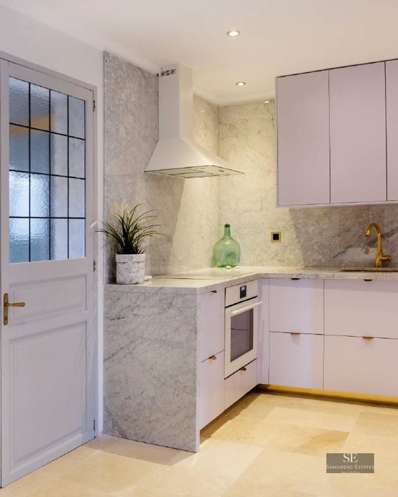 Contemporary kitchen with white cabinets, marble backsplash, gold faucet, and an arched stone window.
