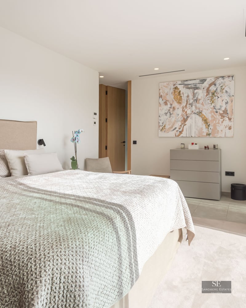 Chambre principale lumineuse avec un grand lit, art abstrait et baies vitrées coulissantes ouvrant sur une terrasse.