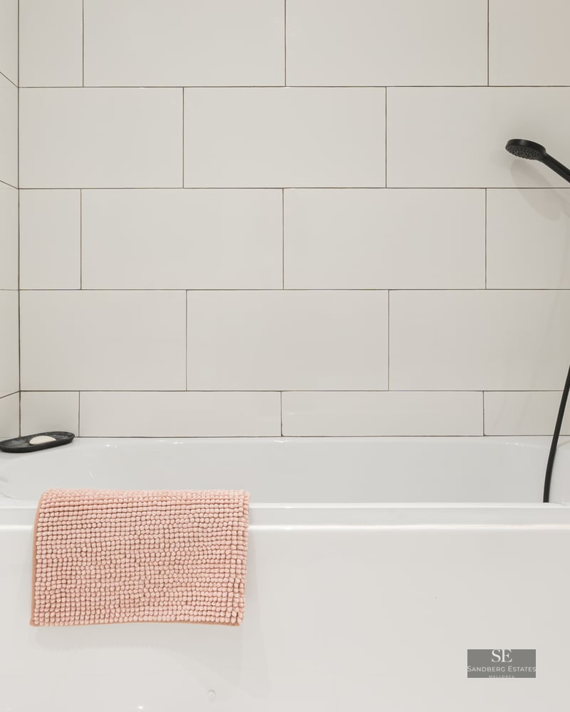 Baignoire blanche, carrelage mural, robinetterie dorée et pommeau de douche noir.