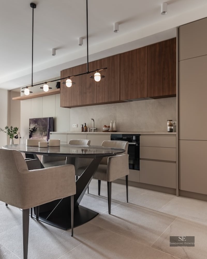 Modern dining area with an oval dark marble table, beige chairs, and a minimalist kitchen with wood accents.