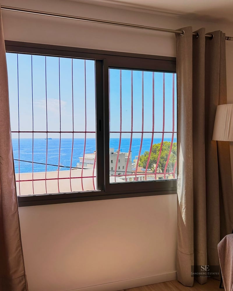 Interior view through a window with security bars looking out over the blue sea and clear sky.