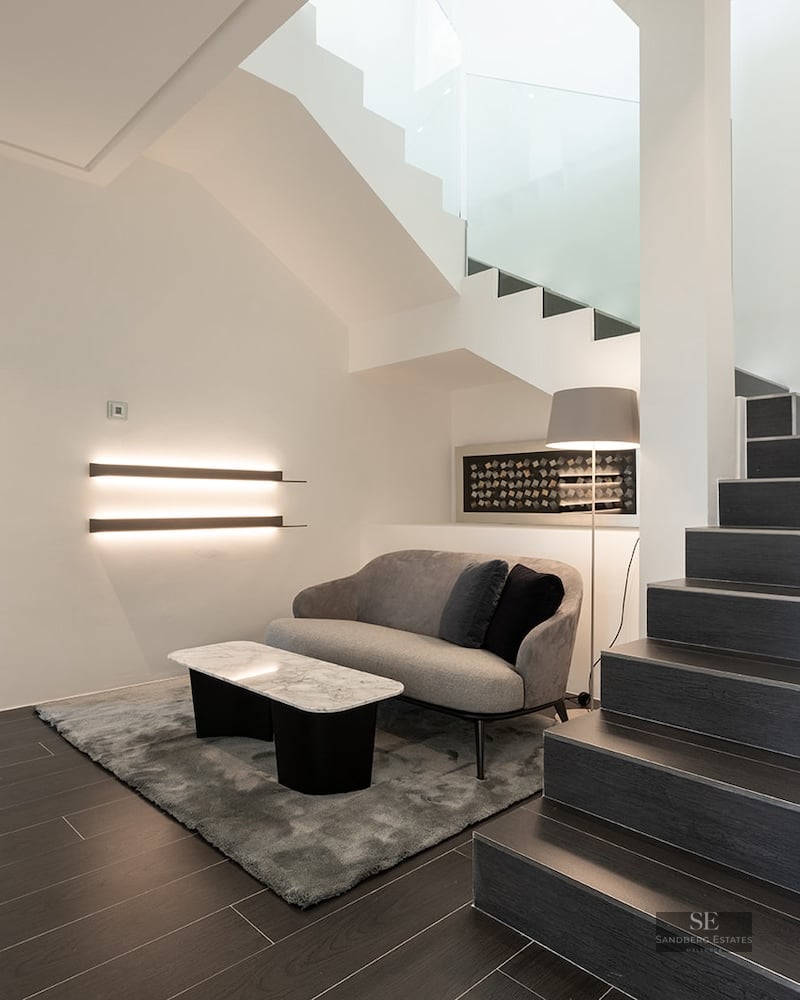 Modern interior featuring dark stairs with integrated LED lighting, a gray sofa, and a marble coffee table.