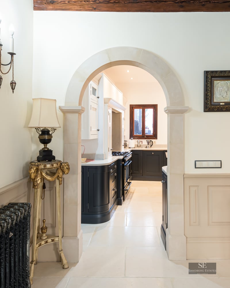 Elegant hallway with a stone archway leading to a kitchen, featuring an ornate radiator and classic wainscoting.