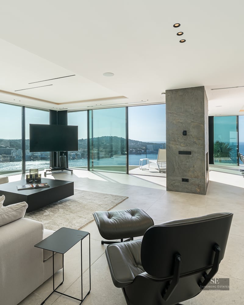 Spacious modern living room with floor-to-ceiling windows overlooking a Mediterranean bay and sea.