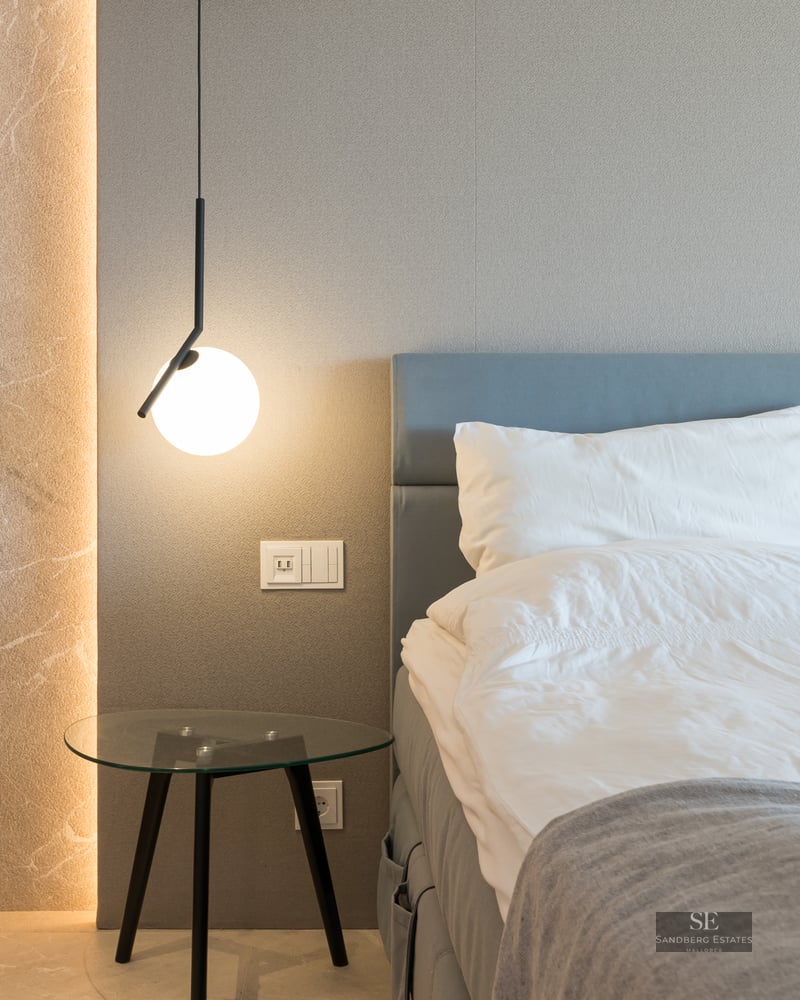 Luxury bedroom featuring a blue headboard, glass table, modern pendant light, and illuminated stone wall detail.