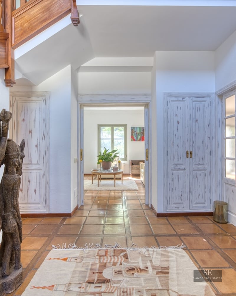 Spacious hallway with terracotta tiles, a large wooden tribal statue, and a wooden staircase leading upstairs.