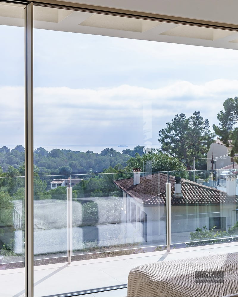 Luxury bedroom with floor-to-ceiling windows overlooking a Mediterranean landscape and the sea.