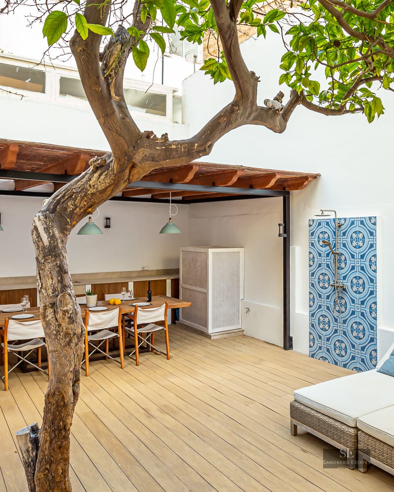 Wooden deck terrace featuring a dining table under a pergola, a large sunbed, and an outdoor shower with blue tiles.