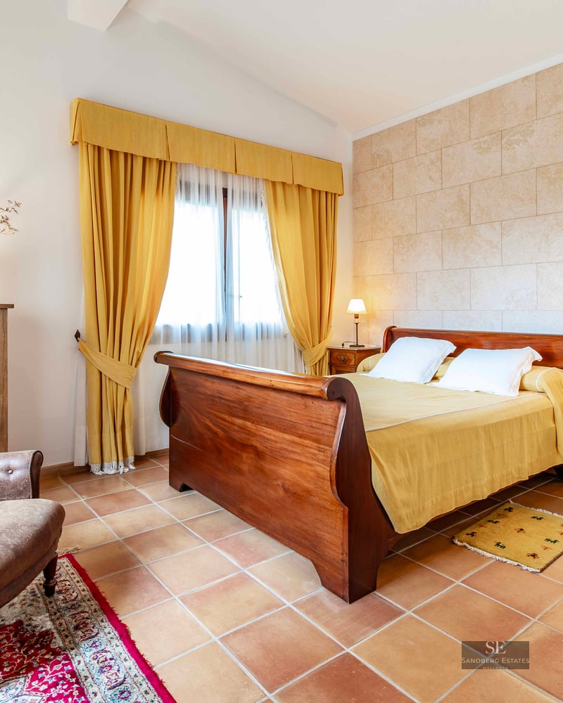 A rustic bedroom with a wooden sleigh bed, terracotta tiles, a leather armchair, and yellow curtains.