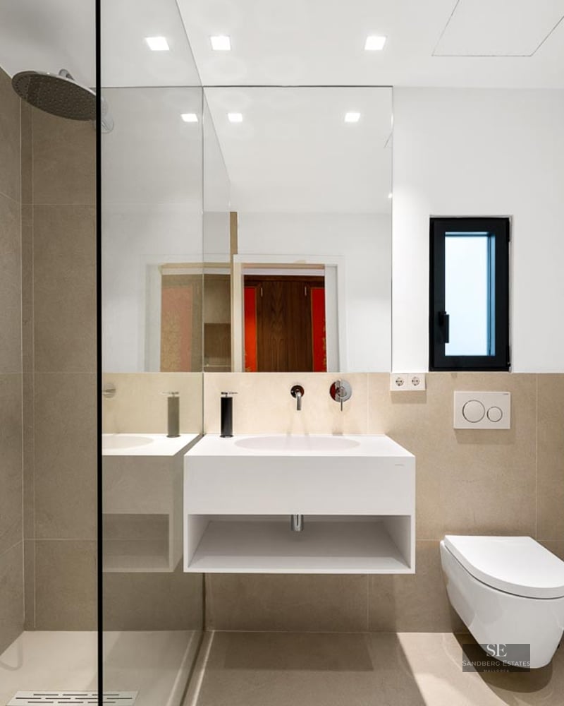 Modern bathroom featuring a glass walk-in shower, floating white vanity, and beige stone-effect tiles.