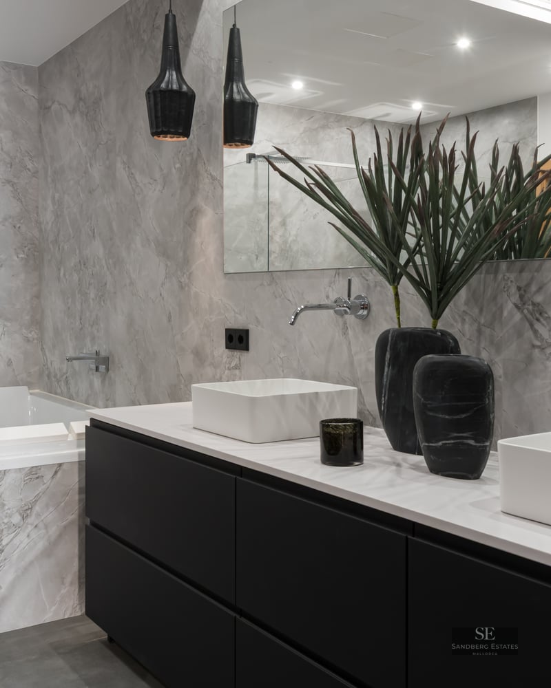 Luxury bathroom with double white sinks, black vanity, marble-tiled bathtub, and a glass-enclosed walk-in shower.