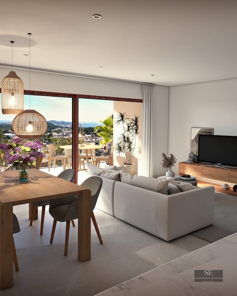 Bright open living room with a grey sofa, wooden dining table, and large glass doors opening to a scenic balcony view.
