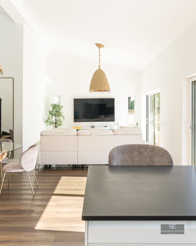 Grand salon à aire ouverte avec canapés blancs, table à manger avec base en racine et grandes baies vitrées.