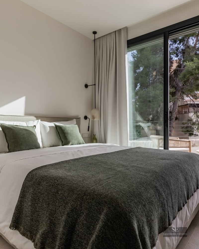 Bright bedroom featuring a double bed with green accents and large glass sliding doors opening to a terrace.