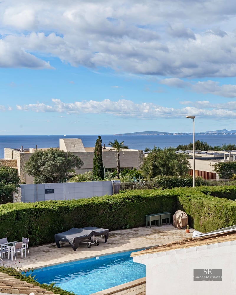 Elevated view of a blue swimming pool in a private garden with a panoramic ocean horizon under a cloudy sky.