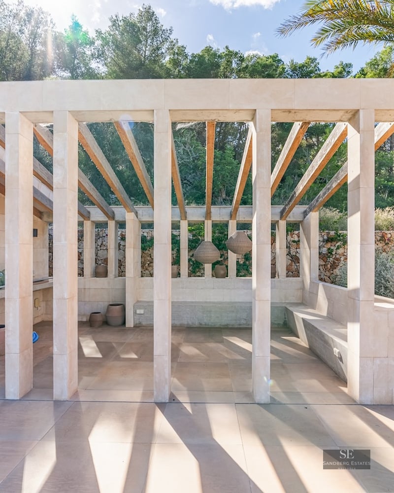 Modern stone pavilion with wooden rafters, outdoor fireplace, and built-in seating surrounded by lush greenery.