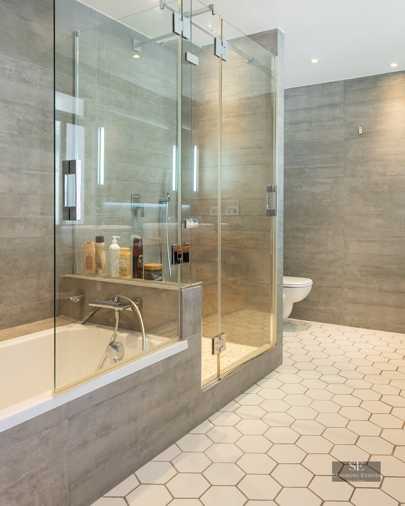 Modern bathroom with white hexagonal floor tiles, a glass-enclosed shower, a bathtub, and grey wall tiles.
