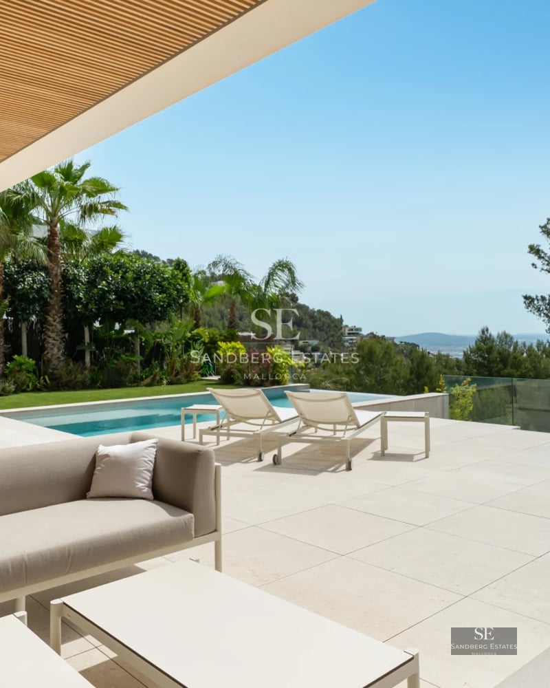 Panoramic view of modern villa with infinity pool and expansive terraces. Sleek and minimalist architecture. Blue sky and lush vegetation.