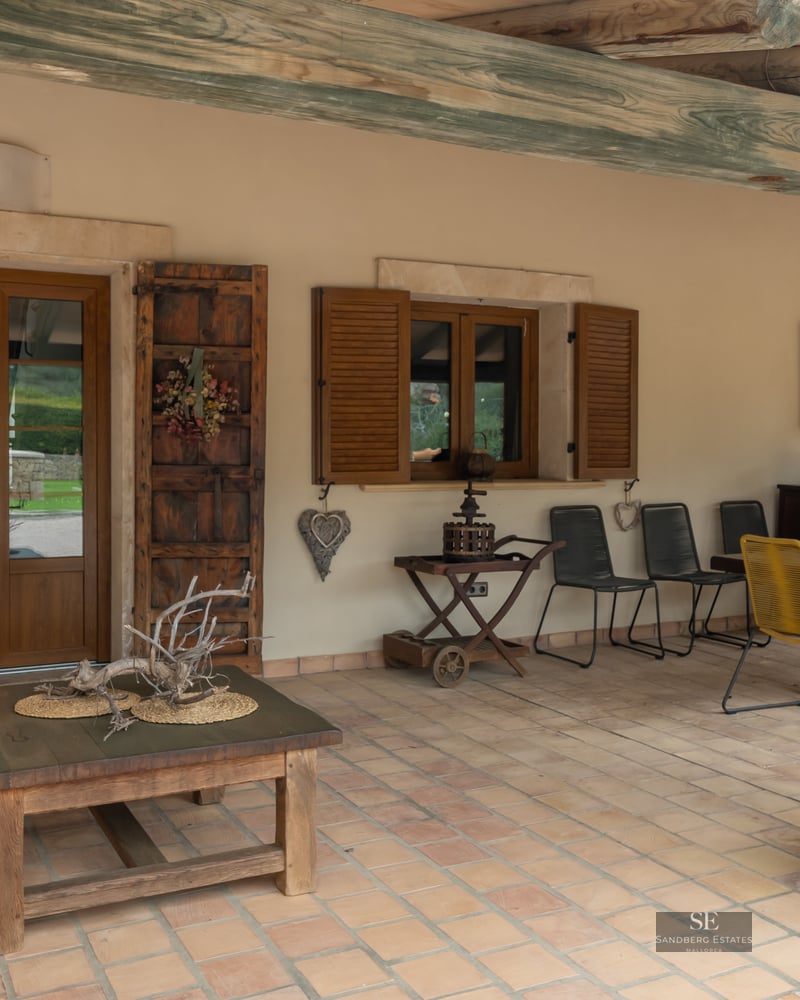 Covered porch featuring terracotta tiles, rustic wooden beams, dining furniture, and light stone walls.