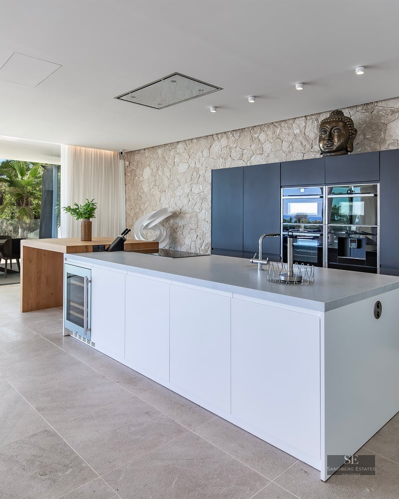 Luxury kitchen featuring a white island, integrated appliances, a rustic stone wall, and glass doors to a terrace.