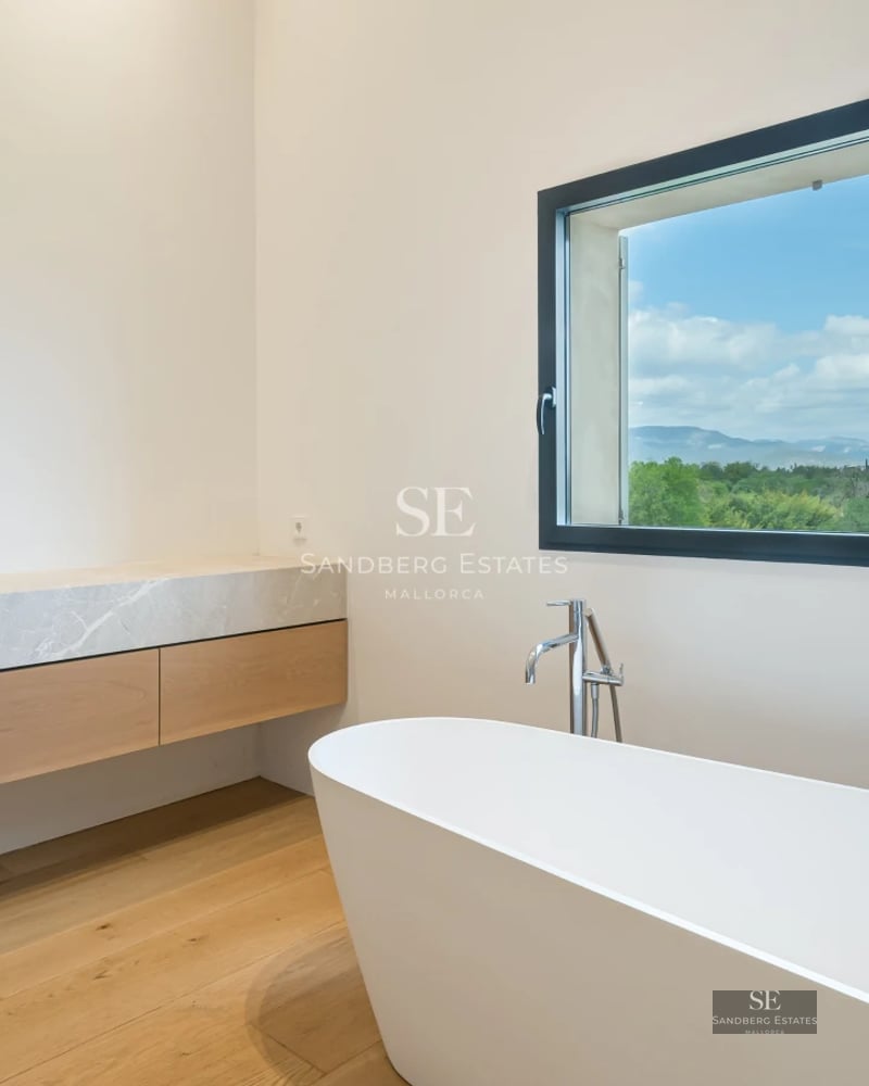 Spacious living room with floor-to-ceiling windows, natural light, wood floors, modern fireplace, and elegant decor. View of lush garden.