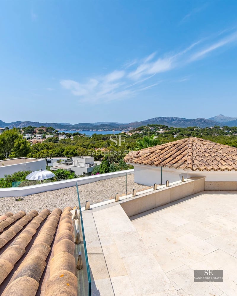 Exterior of a modern villa featuring a pool, large windows, and minimalist design. Lush garden and blue sky.