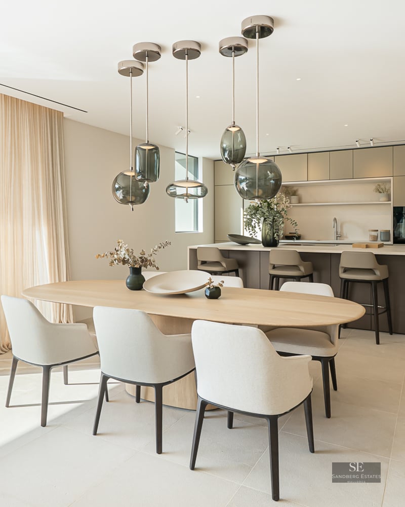 Contemporary dining room with wooden table and glass pendant lights, overlooking an infinity pool and the sea.