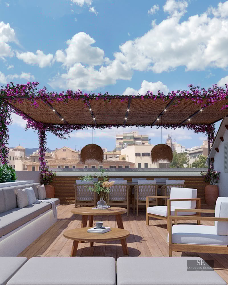 Spacious wooden rooftop terrace with grey sofas, bougainvillea-covered pergola, and outdoor dining area overlooking the city.