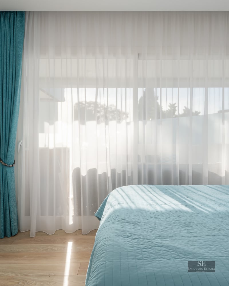 Chambre lumineuse avec lit turquoise, rideaux assortis et grandes fenêtres laissant entrer la lumière naturelle.