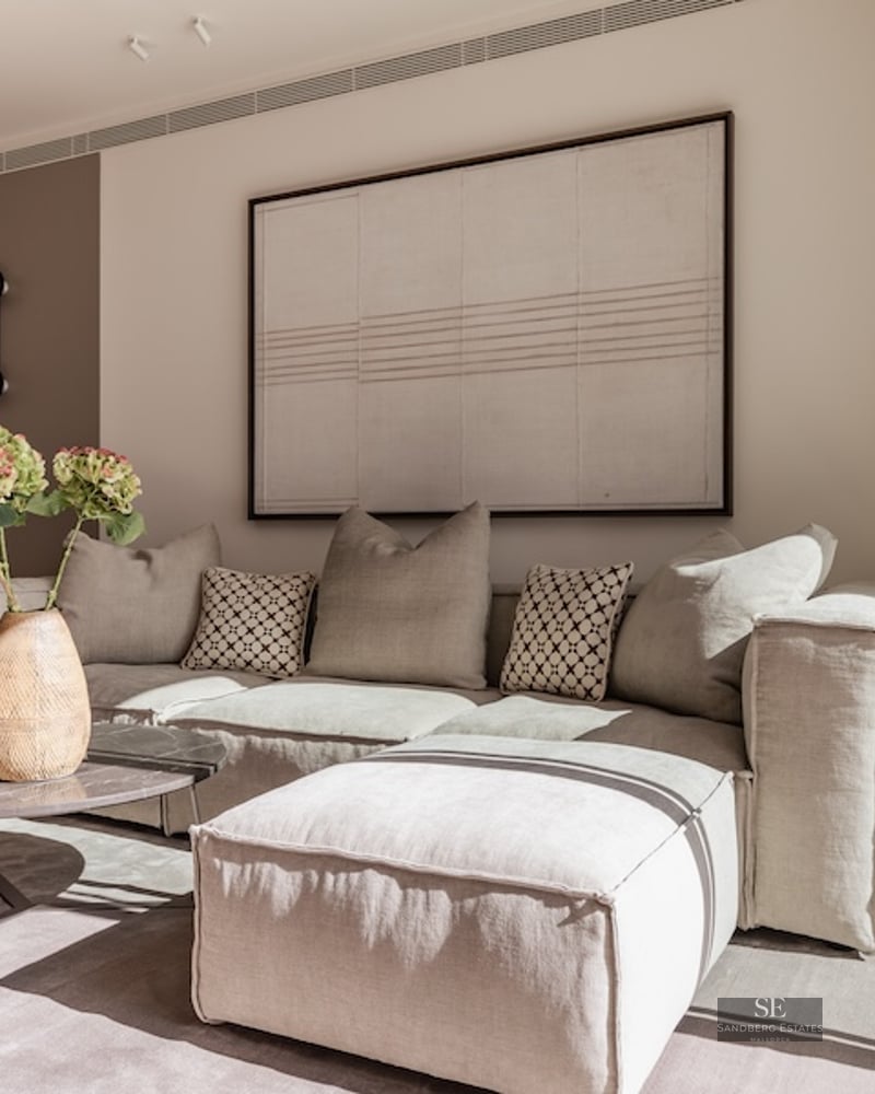 Minimalist living room featuring a large beige sectional sofa, marble coffee table, and large abstract wall art.