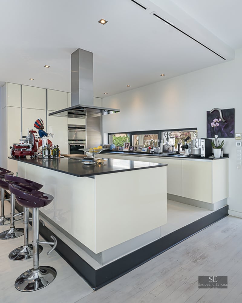Contemporary white kitchen with a large central island, purple bar stools, stainless steel appliances, and home elevator.