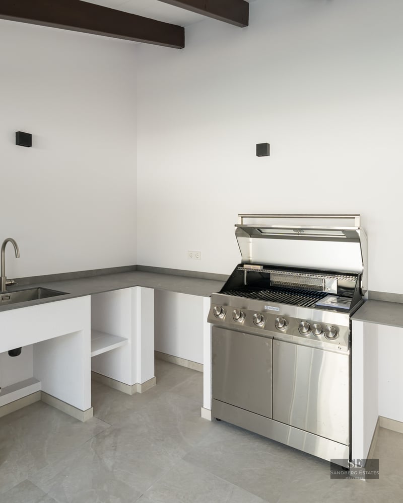 Contemporary outdoor kitchen featuring a stainless steel grill, integrated sink, and sleek gray countertops.