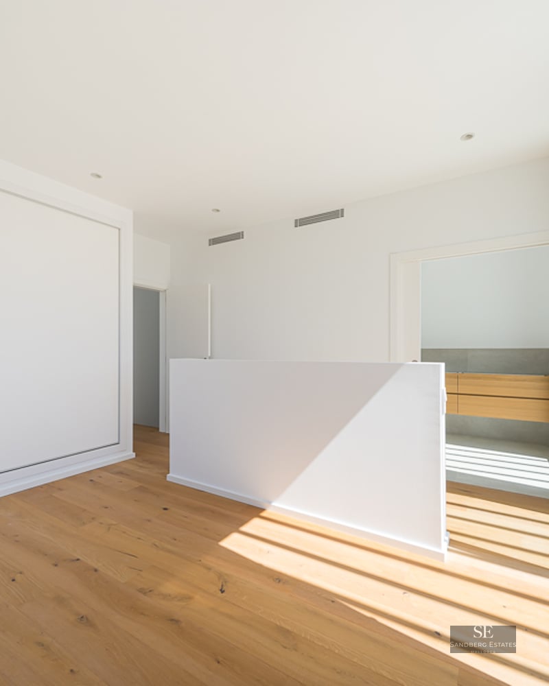 A bright, minimalist bedroom with oak floors, white sliding closets, and large glass doors opening to a terrace.