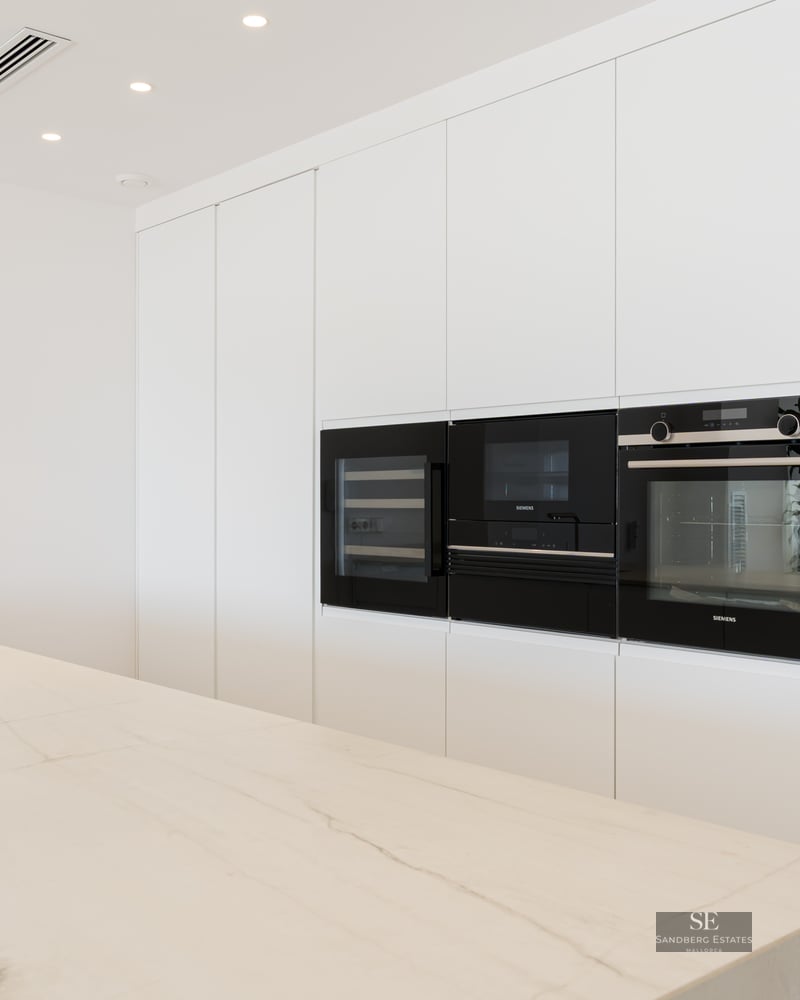 Modern white kitchen featuring a large marble island, integrated sink, and Siemens built-in appliances in handle-less cabinetry.