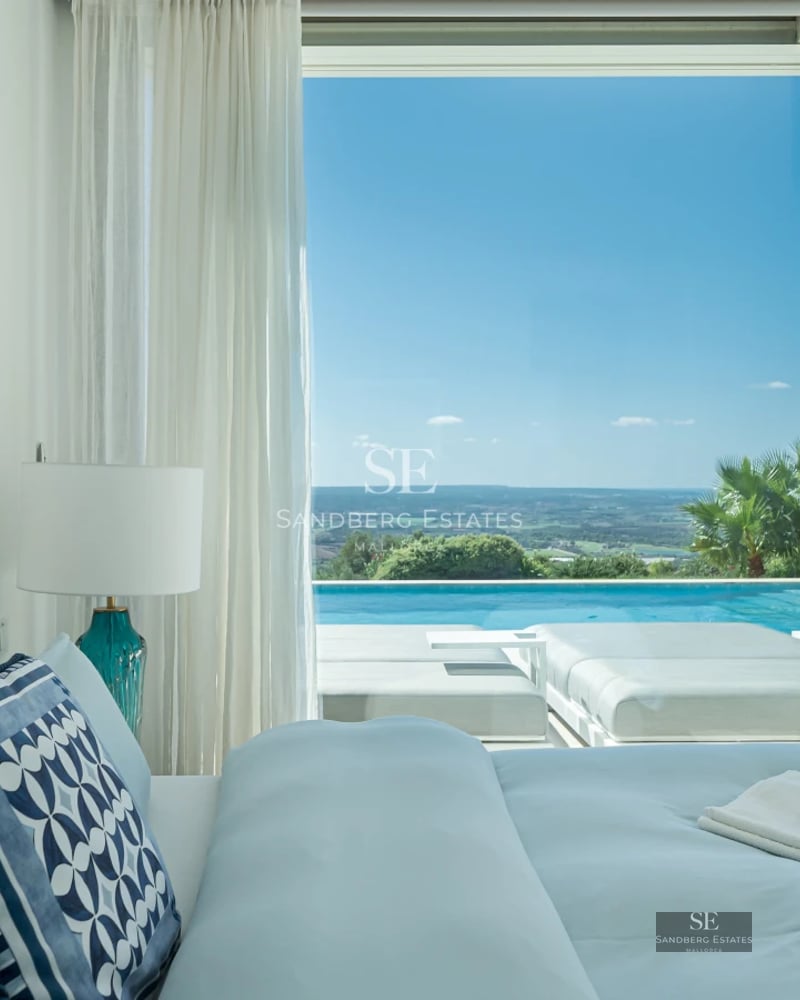 View of a modern pool surrounded by lush greenery and a house with large windows and minimalist design.
