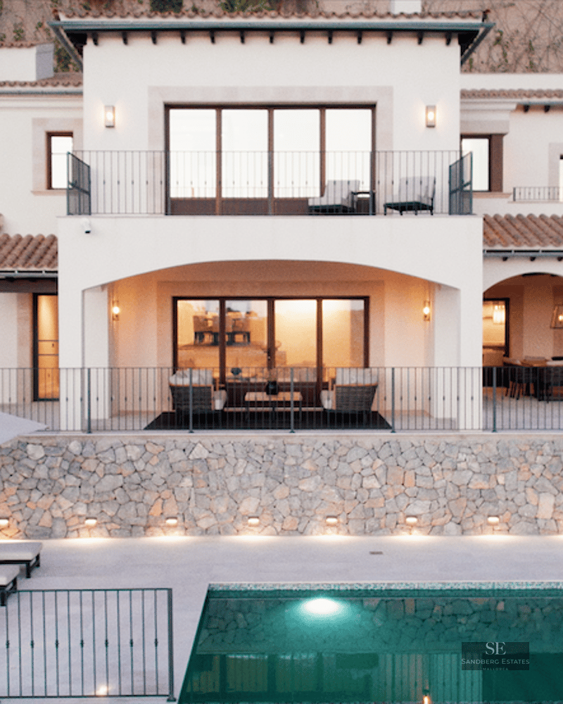 Front view of a white two-story villa at dusk with a swimming pool and loungers in the foreground.
