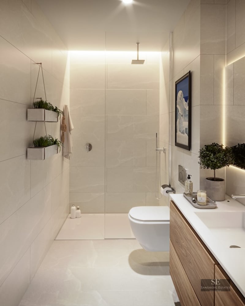 Modern bathroom with beige stone tiles, a glass shower, wood vanity, and a large backlit mirror.