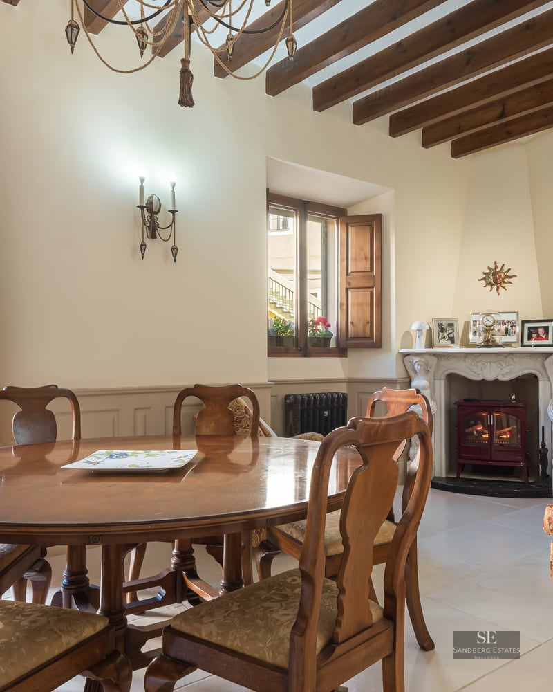 Elegant dining room with wooden table, exposed ceiling beams, and an ornate fireplace leading to an outdoor patio.