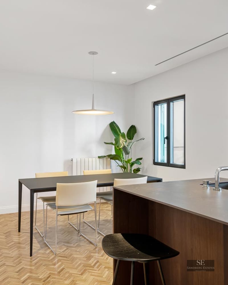 Modern dining room with black table, white chairs, herringbone wood floors, and a kitchen island.