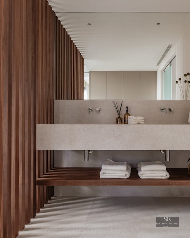 A modern bathroom featuring a floating stone double vanity, a large mirror, and a wall of vertical dark wood slats.