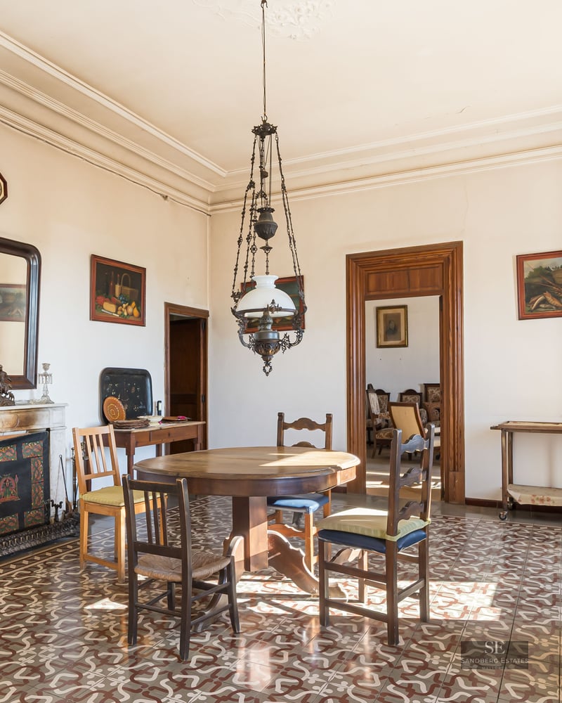 Antique dining room with wooden table, ornate floor tiles, marble fireplace, and high ceilings.