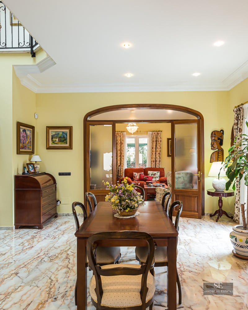 Spacious dining room featuring veined marble floors, classic wooden furniture, and African art decor.