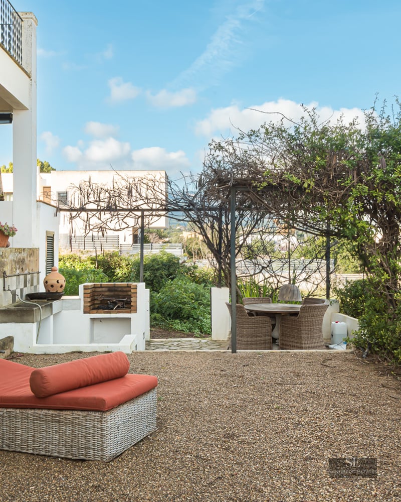 Outdoor terrace featuring a wicker sunbed with orange cushions, a built-in stone grill, and a pergola-shaded dining area.