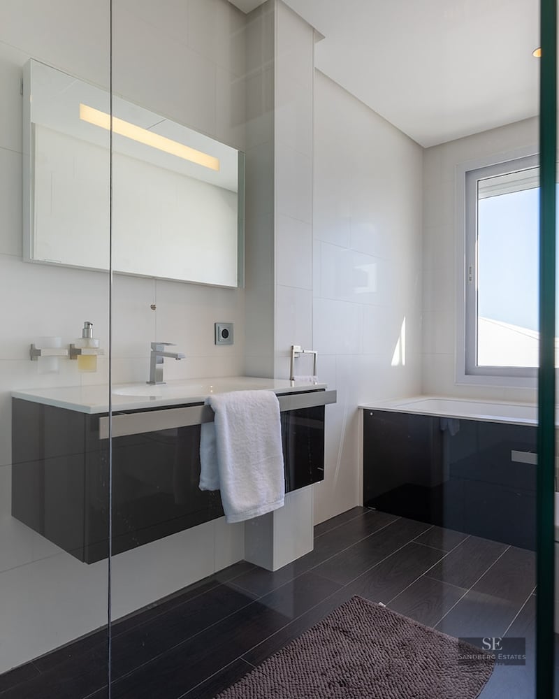 Modern bathroom with white tiled walls, dark floors, a floating vanity, and a bathtub under a large window.