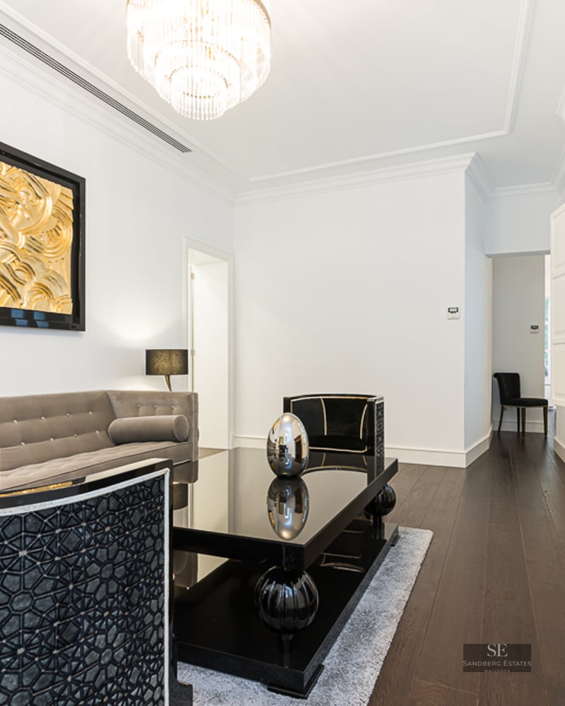Luxury living room with grey velvet sofa, black table, marble fireplace, and gold wall art.
