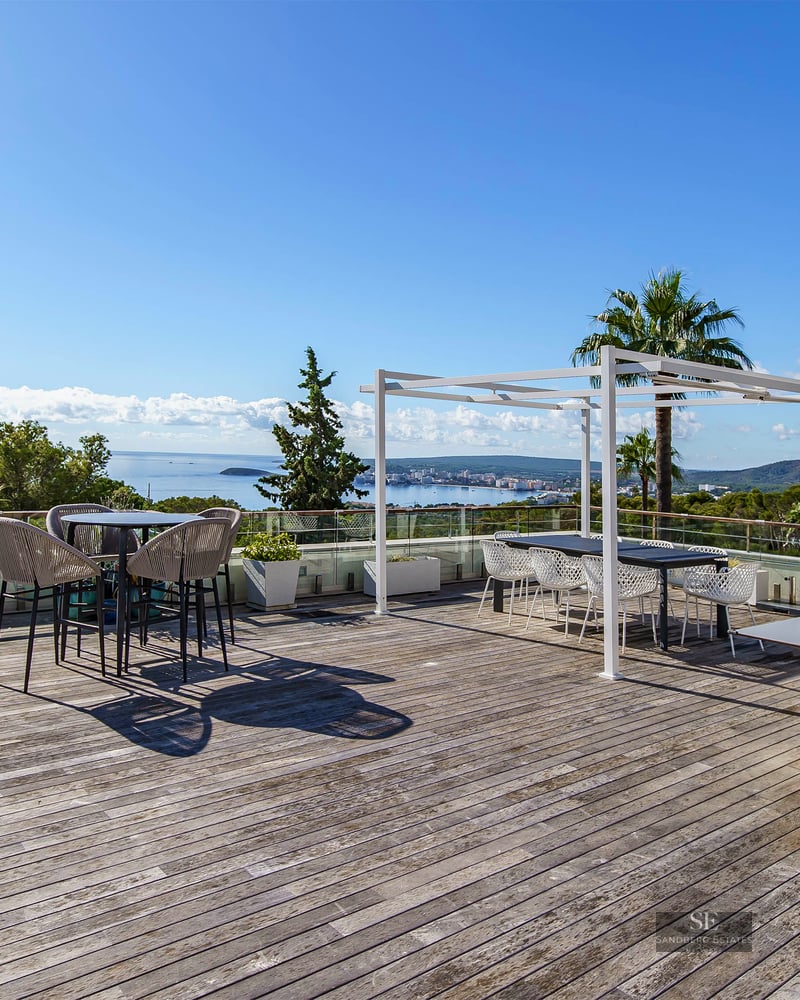 Grande terrasse en bois avec cuisine d'été, coin repas et garde-corps en verre surplombant l'océan.