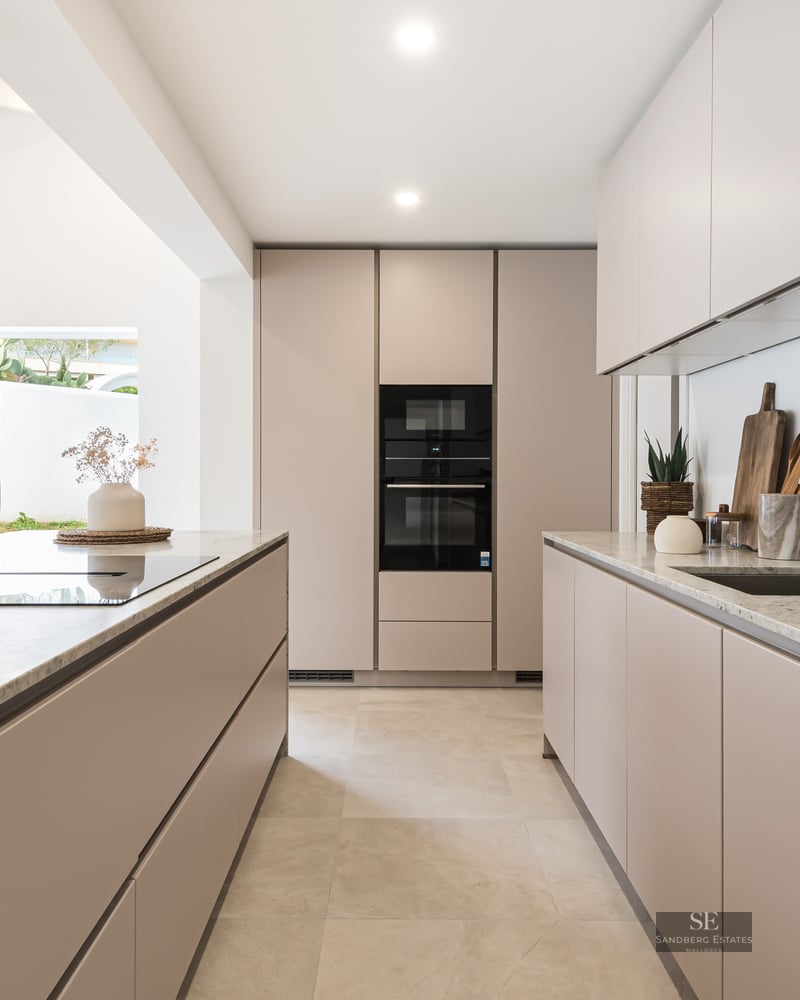 A contemporary beige kitchen featuring granite countertops, a center island, and integrated high-end appliances.