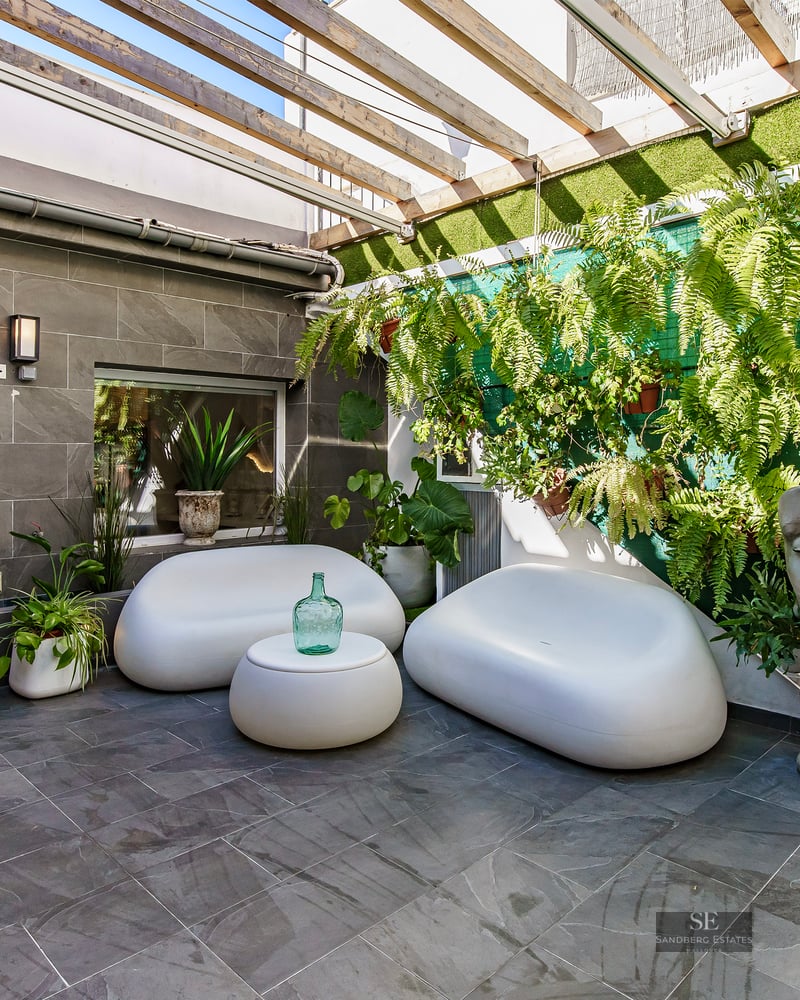 Contemporary patio with white curved sofas, stone tiles, wooden pergola, and a large stone face sculpture.