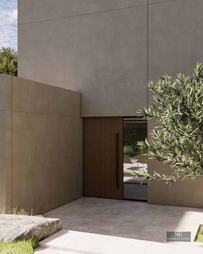 Modern villa entrance featuring beige concrete walls, a wooden door, and a single olive tree in a stone courtyard.