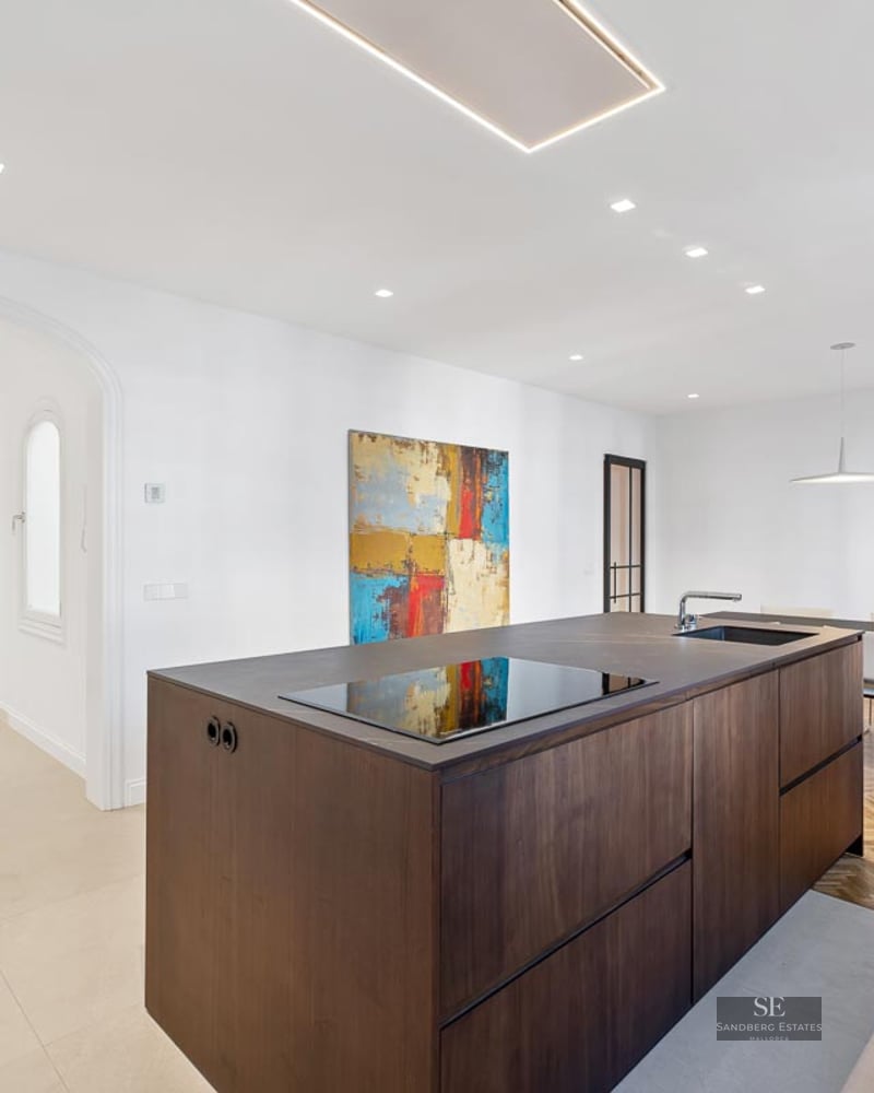 Luxury kitchen featuring a large dark wood island, herringbone flooring, and a modern dining area with a tall plant.